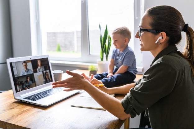 A woman on a Zoom meeting. A toddler sits on the table next to her.