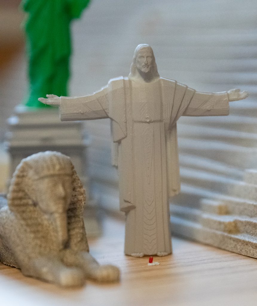 A 3D-printed model of Christ the Redeemer, a statue located in Rio de Janiero, Brazil. There is a small red dot at the feet of the statue that is the size of a human to scale.