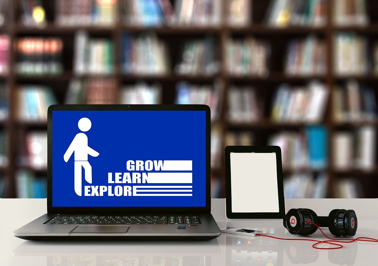 A laptop saying to explore, learn, and grow in front of library shelves.