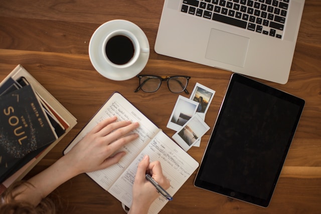 A desk with a laptop, drink, glasses, and a notebook